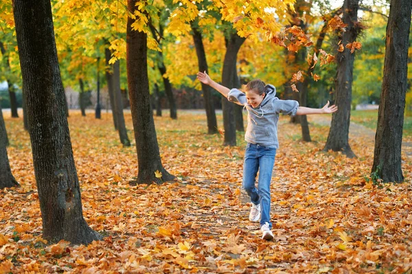 Sonbahar parkında tatil yapan, koşan, gülümseyen, oynayan ve eğlenen bir kız. Parlak sarı ağaçlar ve yapraklar — Stok fotoğraf