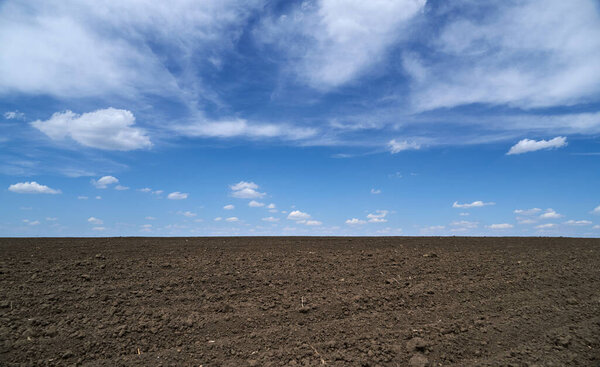 plowed field, soil and clouds of a bright sunny day - concept of agriculture