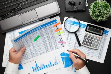 Finansal raporlarla çalışan işadamlarının üst düzey görüşü. Bilgisayarı, defteri, kalemi ve bir sürü şeyi olan modern siyah ofis masası. Düz masa düzeni.