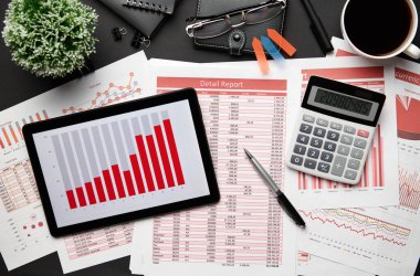 Tablet bilgisayar, mali raporlar, defter, kalem ve bir sürü şeyle modern siyah ofis masasının en üst görüntüsü. Düz masa düzeni.