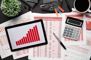 Tablet bilgisayar, mali raporlar, defter, kalem ve bir sürü şeyle modern siyah ofis masasının en üst görüntüsü. Düz masa düzeni.