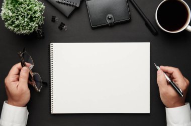 İş adamının ellerinin çalışmasının en üst görüntüsü. Defteri, kalemi ve bir sürü şeyi olan modern siyah ofis masası. Düz masa yerleşimi. Metin için alanı kopyala.