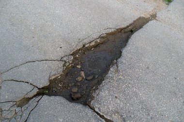 Yolun asfaltında çatlak ve su birikintisi.