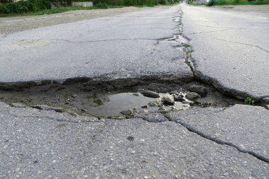 Yolun asfaltında çatlak ve su birikintisi.