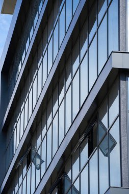 Parlak güneşli bir günde modern bir binanın ön cephesi, mavi gökyüzü ve bulutlar yansıyor yeni binanın güzel dış görünüşü.