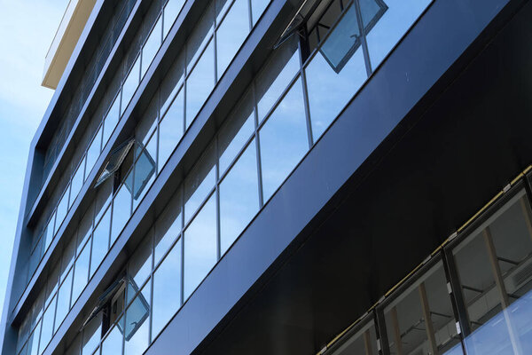 Facade of a modern building on a bright Sunny day, blue sky and clouds reflecting in a glass, beautiful exterior of the new building