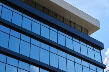 Parlak güneşli bir günde modern bir binanın ön cephesi, mavi gökyüzü ve bulutlar yansıyor yeni binanın güzel dış görünüşü.