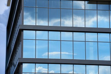 Parlak güneşli bir günde modern bir binanın ön cephesi, mavi gökyüzü ve bulutlar yansıyor yeni binanın güzel dış görünüşü.