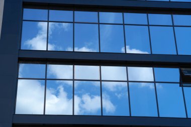 Parlak güneşli bir günde modern bir binanın ön cephesi, mavi gökyüzü ve bulutlar yansıyor yeni binanın güzel dış görünüşü.