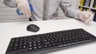 Ofis masasını temizleme ya da dezenfekte etme kavramı - bir işadamı işyerini, bilgisayar klavyesini, evrak klasörlerini, sprey tabanca dezenfektanını, eldivenleri ve kağıt peçeteleri temizler.