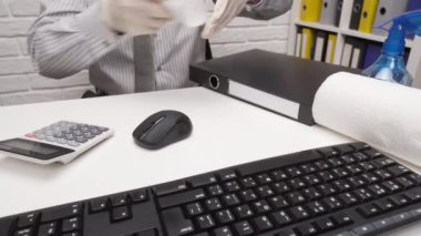 Ofis masasını temizleme ya da dezenfekte etme kavramı - bir işadamı işyerini, bilgisayar klavyesini, evrak klasörlerini, sprey tabanca dezenfektanını, eldivenleri ve kağıt peçeteleri temizler.