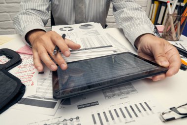 İş analizi ve muhasebe konsepti. Belge, hesap çizelgesi, hesap makinesi ve tablet bilgisayar kullanarak çalışan bir işadamı. Ofis masası kapanıyor..