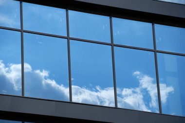 Parlak güneşli bir günde modern bir binanın ön cephesi, mavi gökyüzü ve bulutlar yansıyor yeni binanın güzel dış görünüşü.