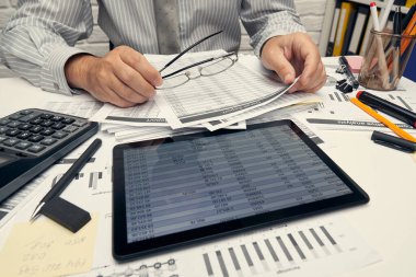 İş analizi ve muhasebe konsepti. Belge, hesap çizelgesi, hesap makinesi ve tablet bilgisayar kullanarak çalışan bir işadamı. Ofis masası kapanıyor..