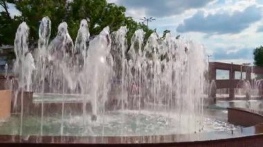 Şehir çeşmesi aydınlık bir yaz gününde, insanlar arkasında yürüyor, kamusal alanda.