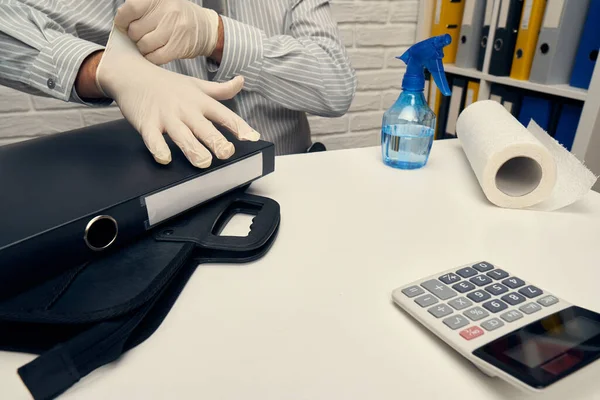 concept of cleaning or disinfecting the office desk - a businessman cleans the workplace, computer keyboard, document folders, uses a spray gun sanitizer, gloves and paper napkins.