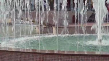 Şehir çeşmesi aydınlık bir yaz gününde, insanlar arkasında yürüyor, kamusal alanda.