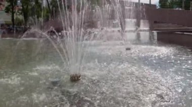 Şehir çeşmesi aydınlık bir yaz gününde, insanlar arkasında yürüyor, kamusal alanda.