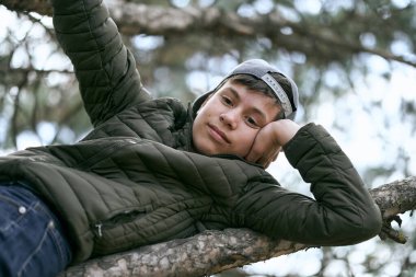 Genç çocuk ağaçta poz veriyor, büyük bir dalda yatıyor ve hayal kuruyor.