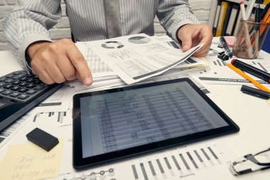 İş analizi ve muhasebe konsepti. Belge, hesap çizelgesi, hesap makinesi ve tablet bilgisayar kullanarak çalışan bir işadamı. Ofis masası kapanıyor..