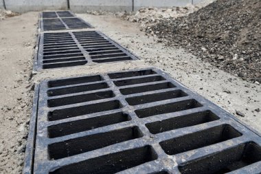 New rainwater grate on the road or sidewalk, installation in concrete. City sewage system for draining water during heavy rain clipart