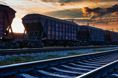 Demiryolu ve vagonlar güzel bir gün batımında, dramatik gökyüzü ve güneş ışığı