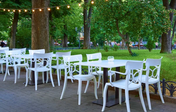 露天街道咖啡馆 白色的椅子和桌子 装饰照明 城市公园和步行的人 — 图库照片