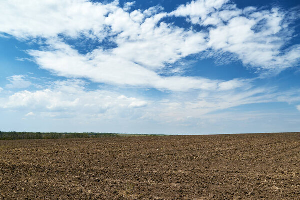 plowed field and blue sky, soil and clouds of a bright sunny day - concept of agriculture