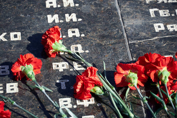 flowers on the memorial to fallen soldiers, red carnations on black marble, Russian text of soldiers military rank - sergeant,major, colonel,Lieutenant Colonel, private, corporal