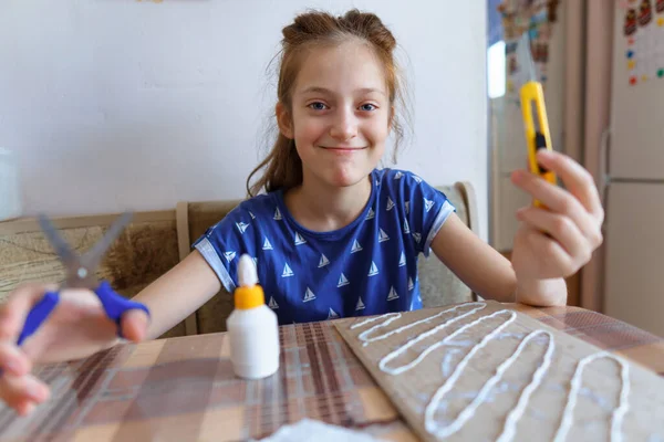 女の子は工芸品や接着剤の段ボールを作って家のキッチンに座り — ストック写真