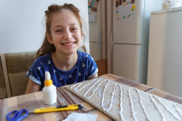 the girl makes crafts, glues cardboard, sits in the home kitchen