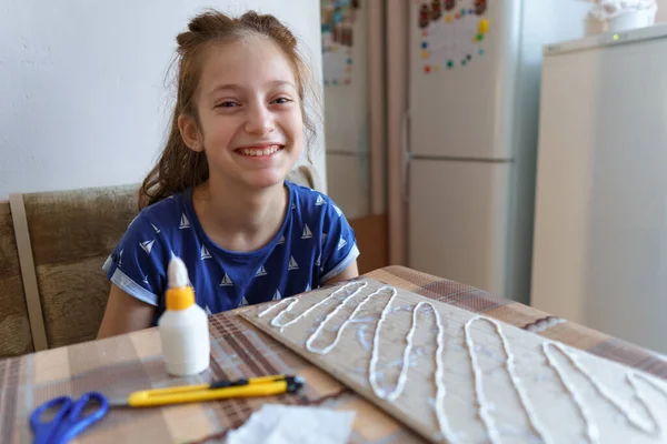 女の子は工芸品や接着剤の段ボールを作って家のキッチンに座り — ストック写真