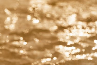 Odaklanmamış su yüzeyi, arka plan olarak güneş ışığı bokeh, altın rengi ton