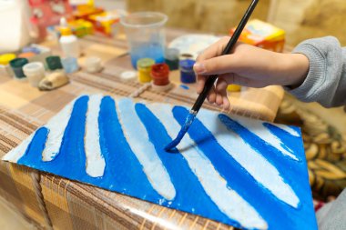 Kız mavi gouache karton çiziyor, soyut bir arkaplan çiziyor, ev mutfağında oturuyor.