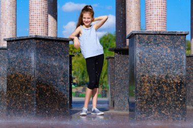 Şehir parkındaki çardakta düşen su damlalarıyla oynayan bir kız, aydınlık bir yaz günü.