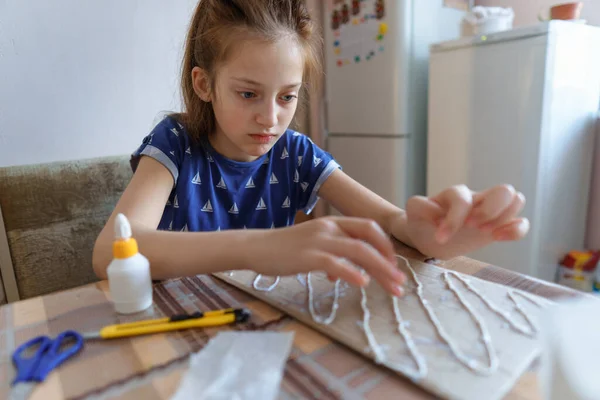 the girl makes crafts, glues cardboard, sits in the home kitchen