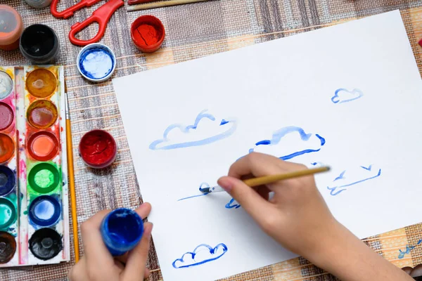 a girl drawing watercolor blue clouds on a blank white paper, artistic creation at home, makes creative artwork