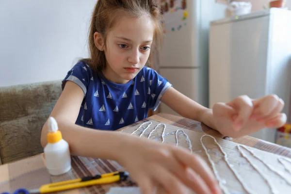 女の子は工芸品や接着剤の段ボールを作って家のキッチンに座り — ストック写真