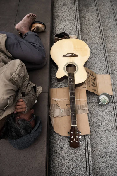 老乞食やギターで近代的な都市の階段で寝ているホームレスの汚い男の平面図 ボウル ヘルプ テキストとダン ボールにお金を寄付します 天気が悪いと冬の間に冷たい感じ — ストック写真