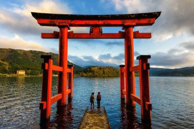 Japanese couple at red Torii gate of Hakone shrine located on lake Ashi, Japan. Gateways entrance to Shinto shrines and famous tourist landmark. clipart