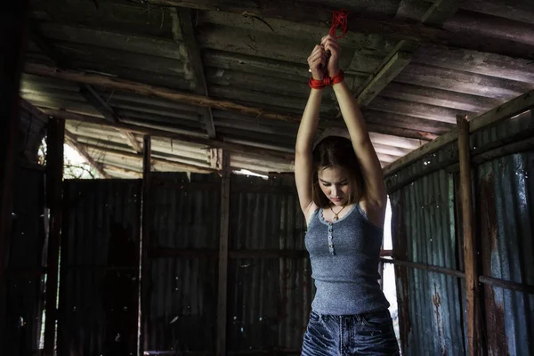 Terk edilmiş evde kirli çatı tavanda kırmızı iple bağlı güzel Asyalı kız eller düşürmek. Rehine kavram ya da erkek soyguncu kaçırdı. Cinsel istismar, tecavüz, Crimical, kurban.