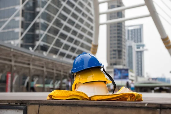 Safety helmet hats and yellow worker dress on footpath with blurred modern city  background. Engineering and construction equipment with copy space text. Engineer heavy industry Project