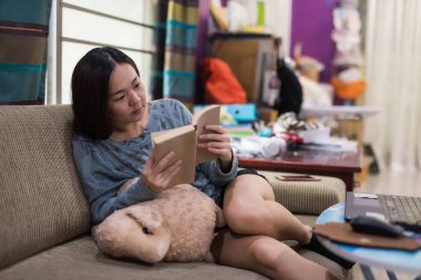 Asyalı kadın kanepe oturma odası kurgu metin kitap okumak rahatla. Eğlence ve hobi kavramı içinde ev.