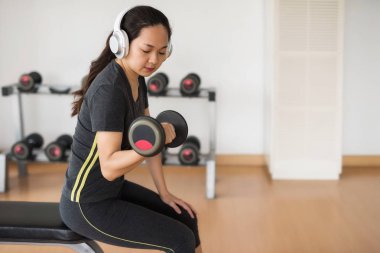 Fitness Asyalı kadın dumbbell ile iş çıkışı ve kulaklık spor salonunda tarafından müzik dinle. Sağlıklı kız yoğun bir eğitim vardır ve Spor donatımı tutun. Bina el ve kol. Spor yaşam tarzı kavramı.