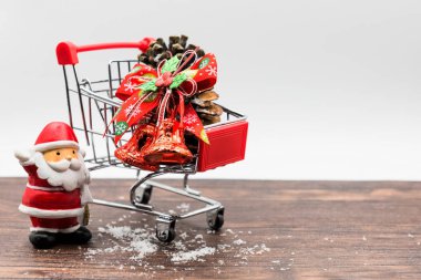 X'Mas kırmızı santa claus, bell, çam kozalakları, kar üzerinde eski ahşap masa ve metin kopyalama yeri olan beyaz arka plan üzerinde kırmızı küçük alışveriş sepeti. Noel dekorasyon düzenlemesi.