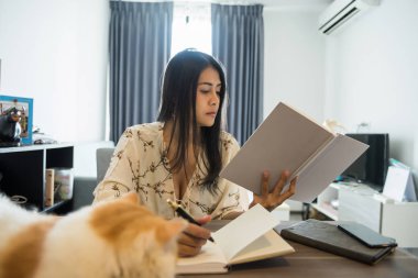 Genç güzel Asyalı kız öğrenci ders kitabı ve yazma tablo ile şirin egzotik stenografi kedi okudunuz. Eğitim ve çok çalışkan kadın evde.