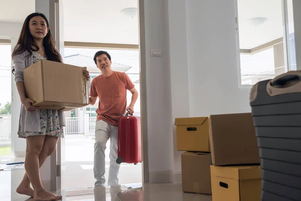 Happy Asian husband carry luggage and walk into new house while female wife carry box. moving with many boxes and luggage. First home to start couple life.