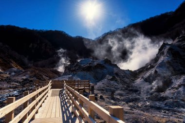 İz veya ahşap patika kükürt puslu, mavi gökyüzü ve gündoğumu ile Noboribetsu, Hokkaido, Japonya'nın yürümeye Jigokudani Cehennem Vadisi.
