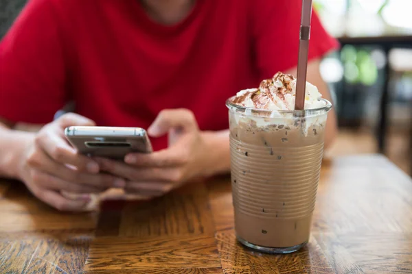 Man in cafe using smartphone to chat and play social media near Ice mocha coffee with whip cream in cafe. Relax lifestyle