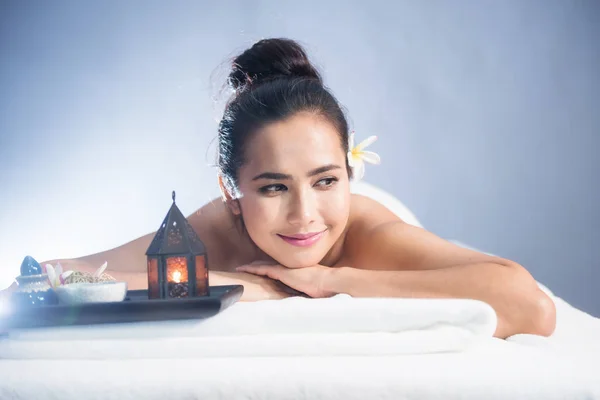 portrait of young happy Asian beautiful woman relax in spa. Body care treatment. Cute girl having Thai oil massage on bed with candle and white Plumeria on bed with copy space for text.